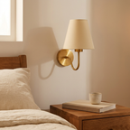 Gold fabric shade wall lamp above a bedside table