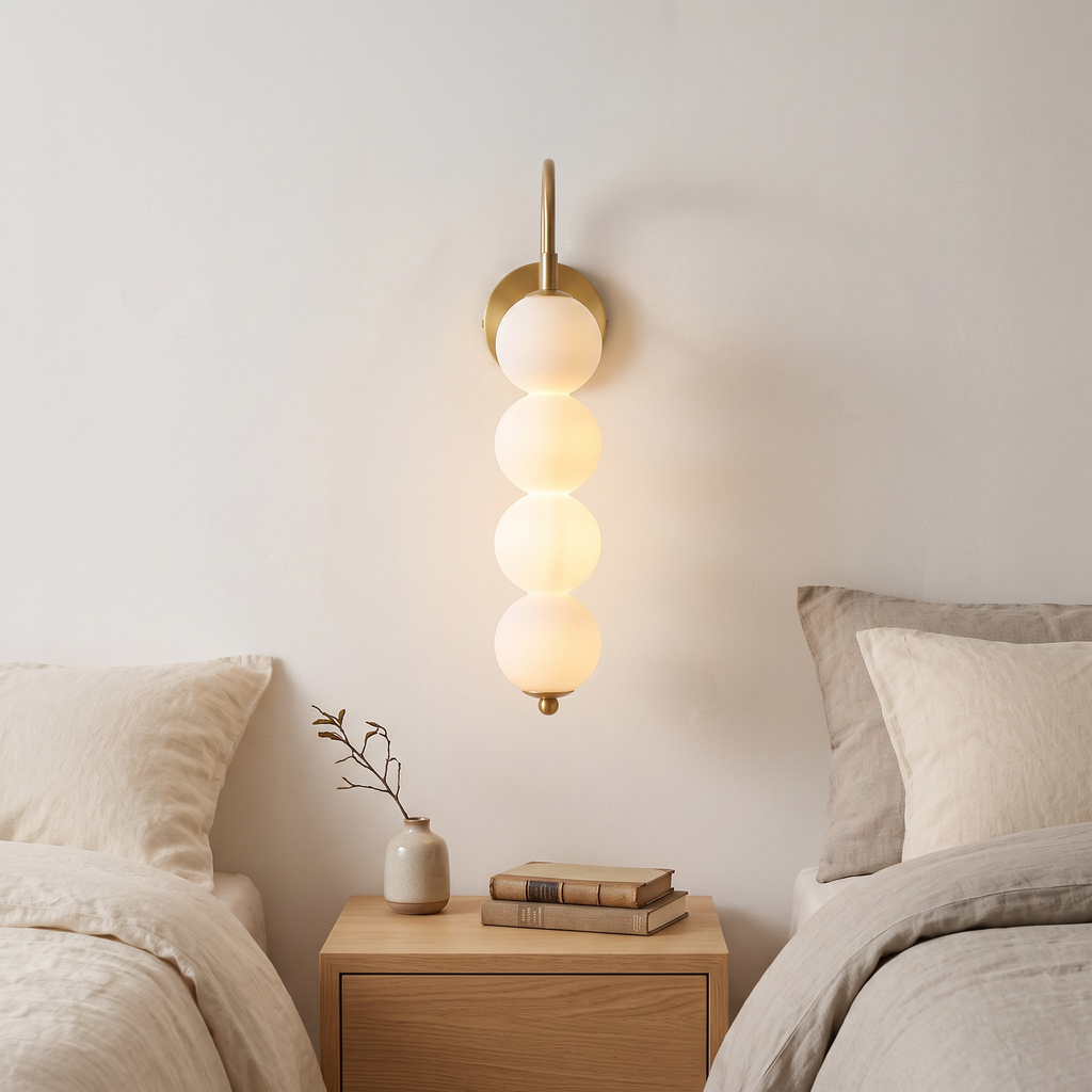 Stacked globe wall lamp with four opal globes lit beside a bed in a calm Nordic bedroom